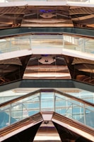 The image features the interior view of a modern architectural structure with reflective metal surfaces and glass panels. The design incorporates geometric shapes and angles, creating a visually dynamic pattern with reflections and light plays.