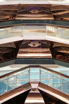 The image features the interior view of a modern architectural structure with reflective metal surfaces and glass panels. The design incorporates geometric shapes and angles, creating a visually dynamic pattern with reflections and light plays.