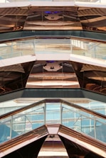 The image features the interior view of a modern architectural structure with reflective metal surfaces and glass panels. The design incorporates geometric shapes and angles, creating a visually dynamic pattern with reflections and light plays.