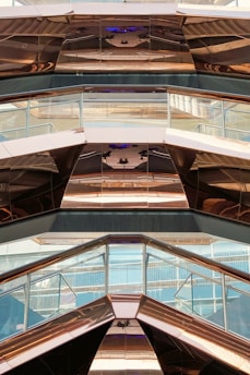 The image features the interior view of a modern architectural structure with reflective metal surfaces and glass panels. The design incorporates geometric shapes and angles, creating a visually dynamic pattern with reflections and light plays.