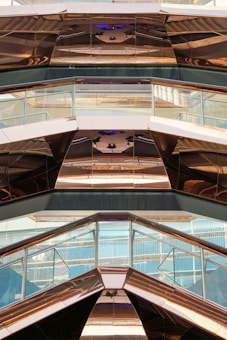 The image features the interior view of a modern architectural structure with reflective metal surfaces and glass panels. The design incorporates geometric shapes and angles, creating a visually dynamic pattern with reflections and light plays.