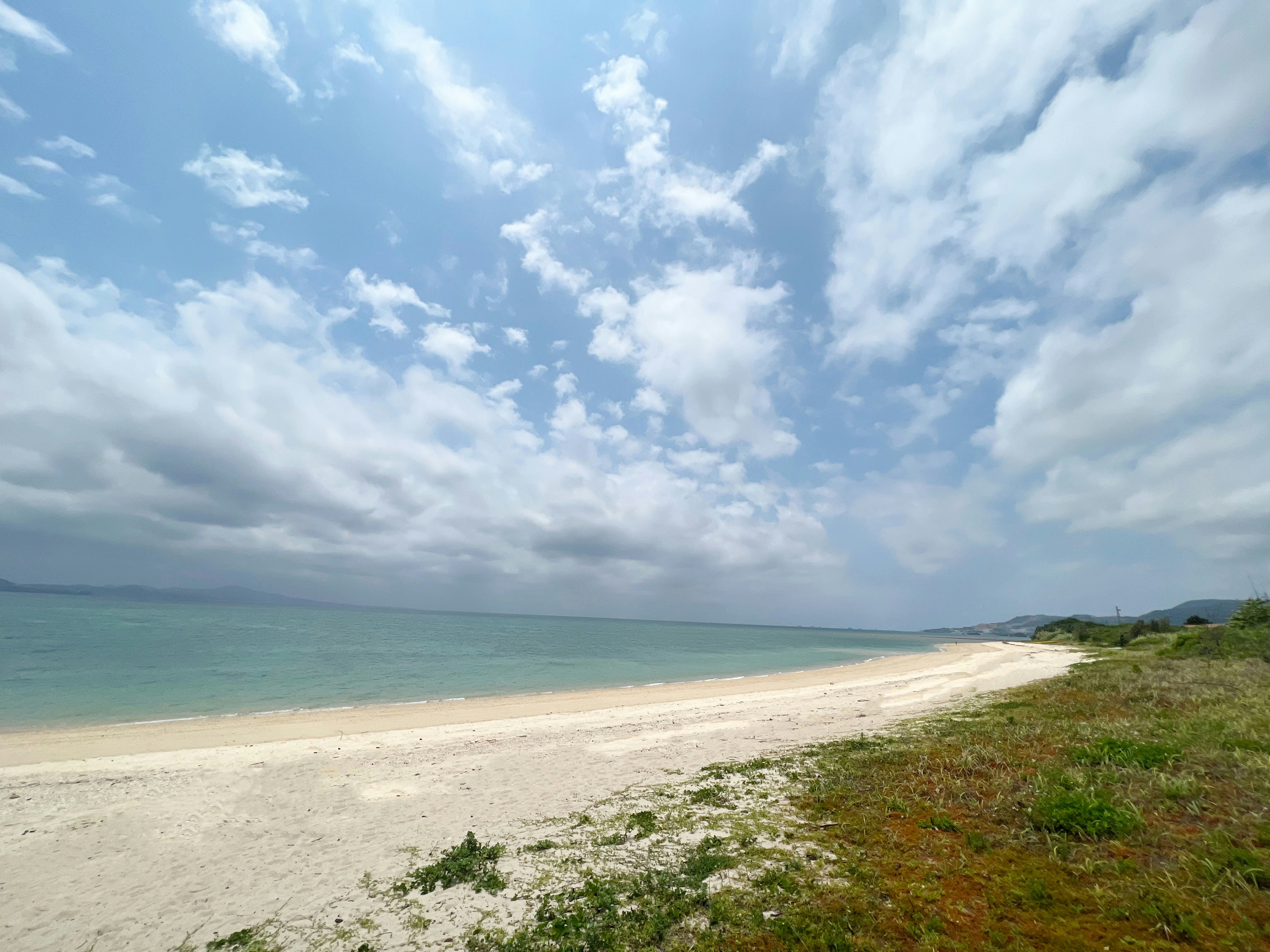 Pristine white sandy beach with calm turquoise water, clear blue sky with wispy clouds, peaceful Florida coastline