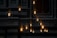 Multiple Edison-style light bulbs hang in a dimly lit area, casting a warm glow. The background consists of a blurred architectural structure with vertical stripes.