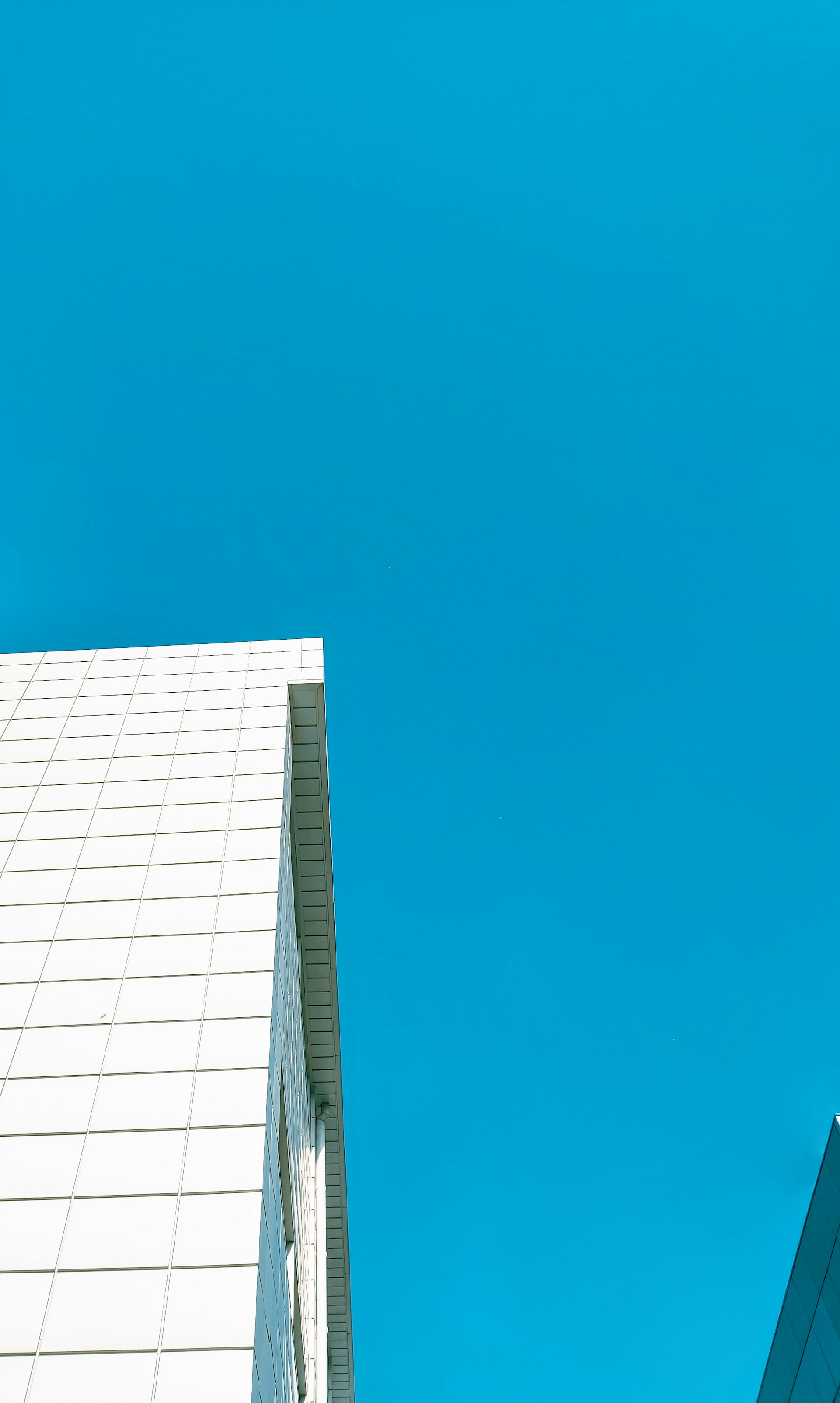 A modern white facade of a building showcasing sharp angles and smooth surfaces under a clear sky.
