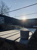 A steaming cup of coffee resting on a rustic wooden picnic table overlooking a misty trail.