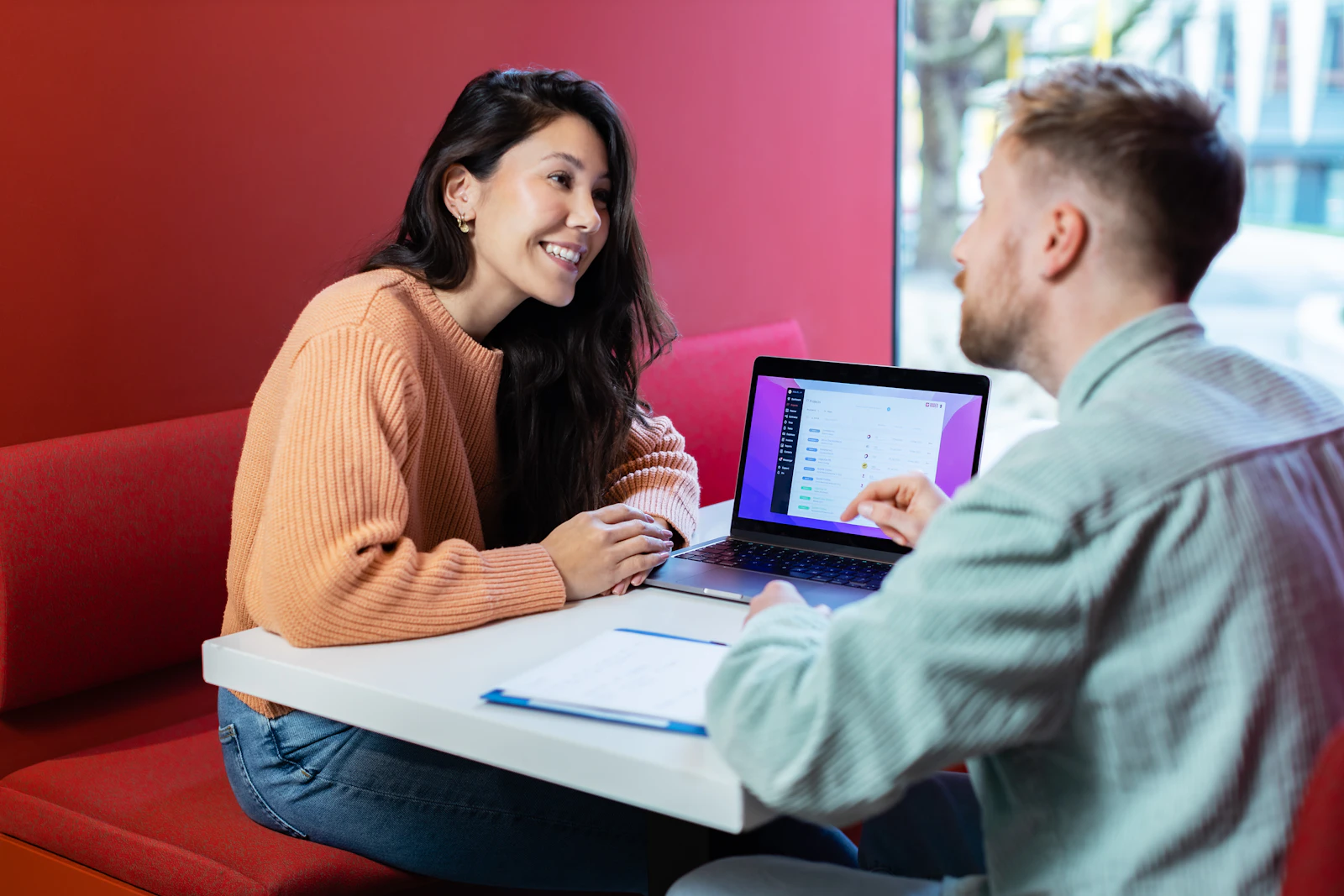 Two people reviewing a status table on a laptop in a bright office