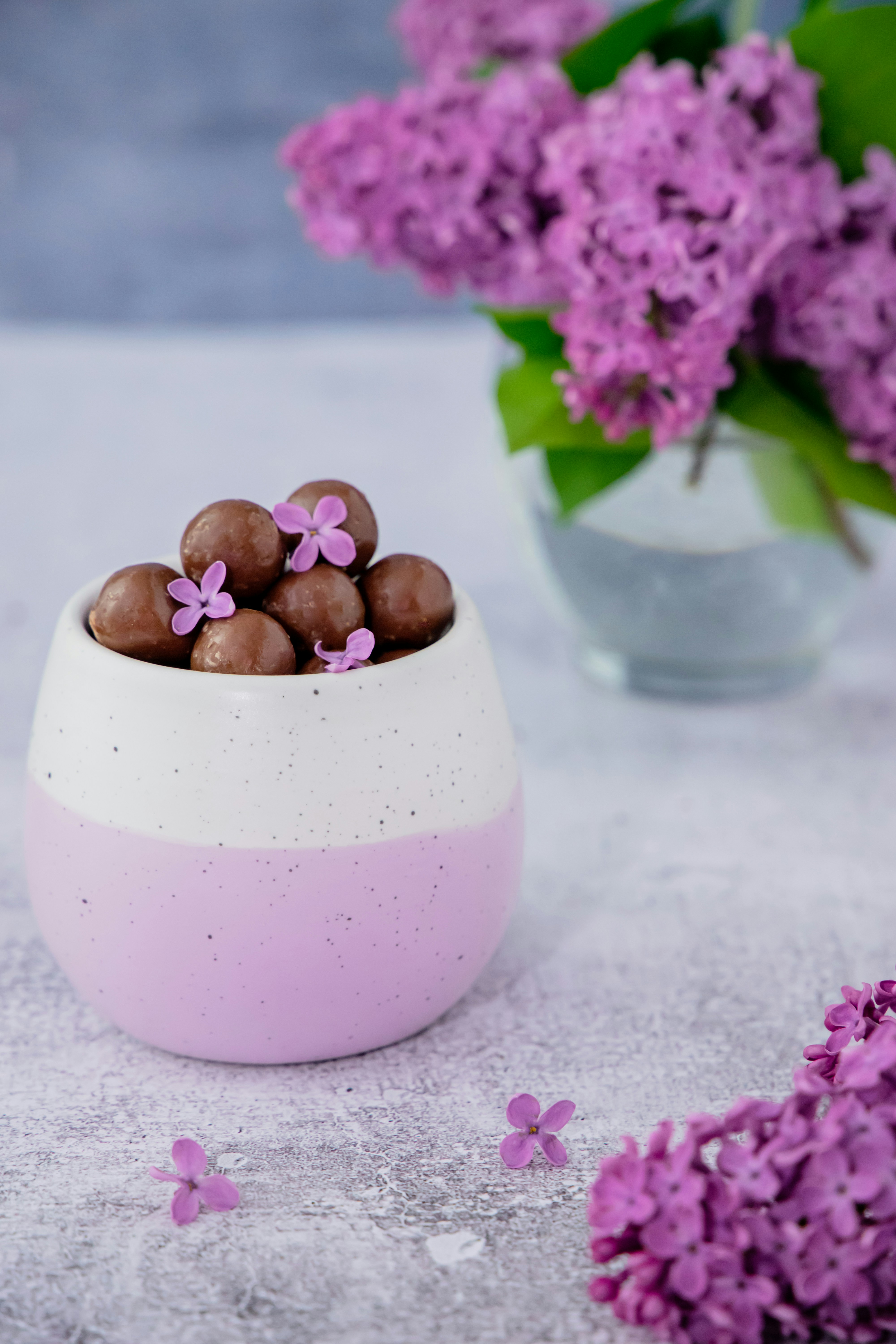 eine weiße Schale gefüllt mit Pralinen neben lila Blumen