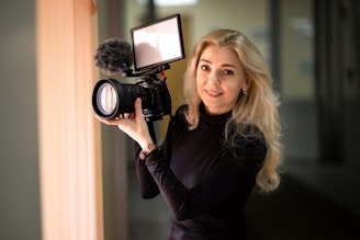 A friendly team member at wigleymedia.com smiling while holding a camera and microphone in a creative studio.
