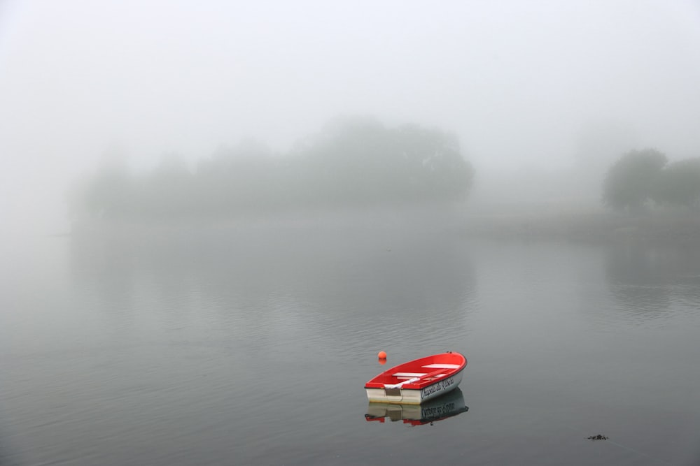 a red boat floating on top of a lake covered in fog