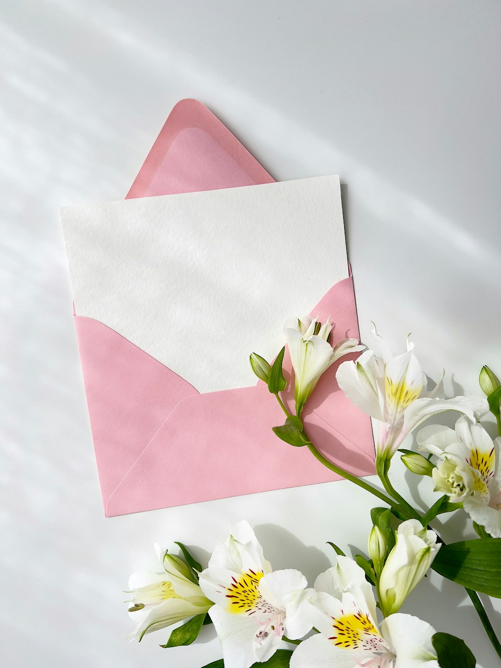 a pink envelope and white flowers on a white table