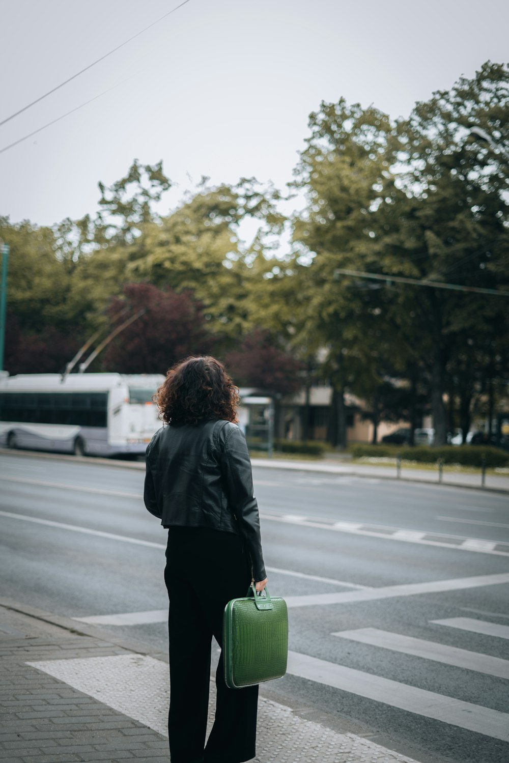 a woman with a green suitcase waiting at a crosswalk