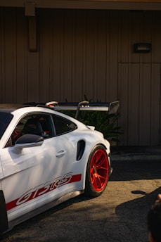 Red Porsche 911 GT3 with custom red and white accents parked against a black gradient background.