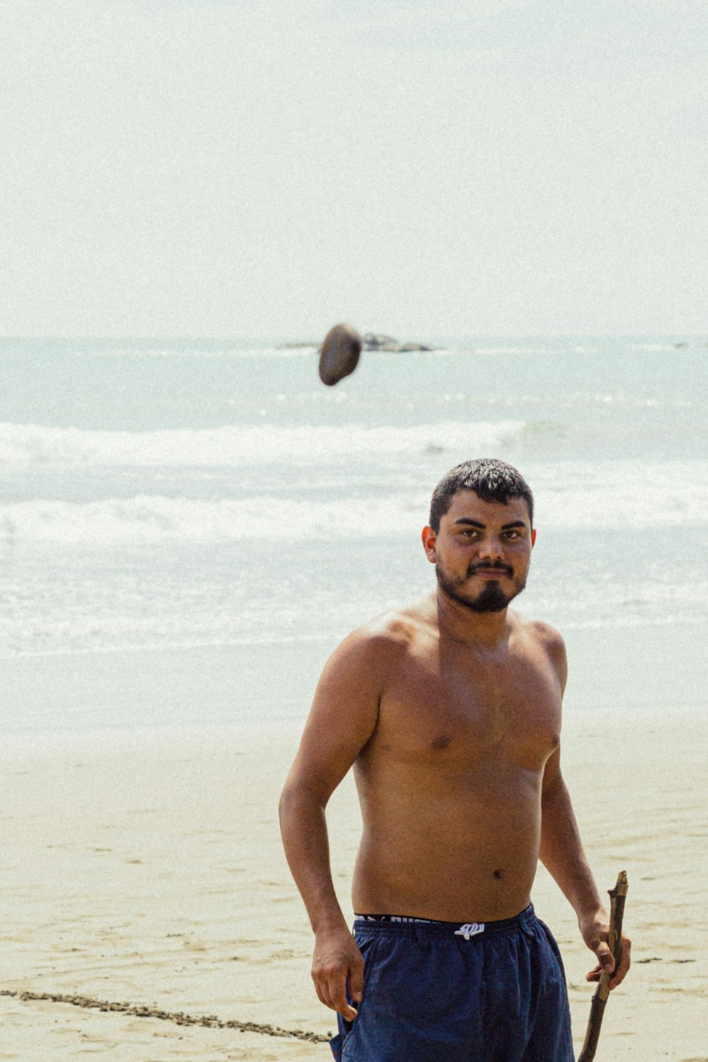 a man standing on a beach holding a stick and a frisbee