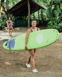 a woman holding a green surfboard in front of a hut