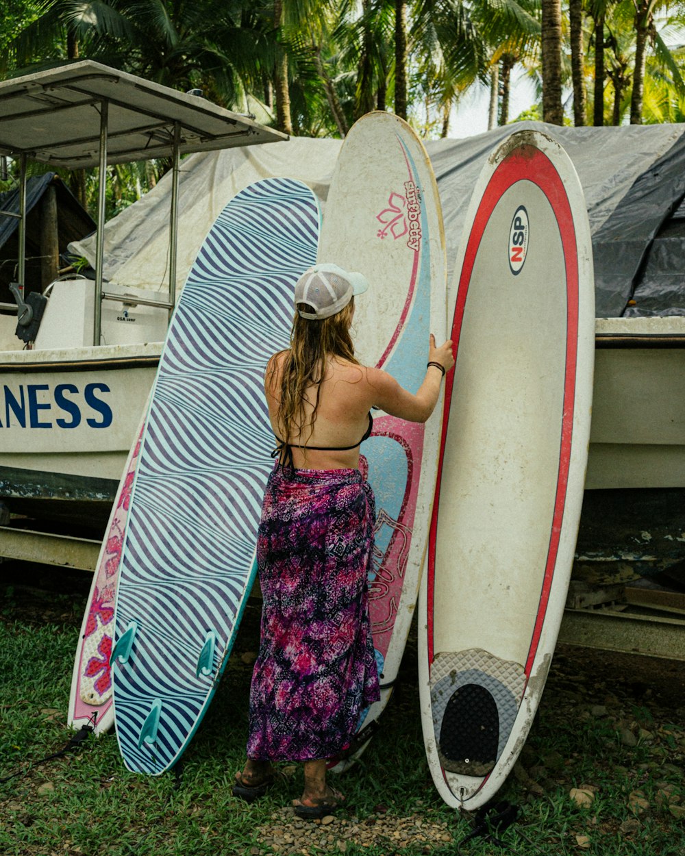 a woman holding two surfboards next to a boat