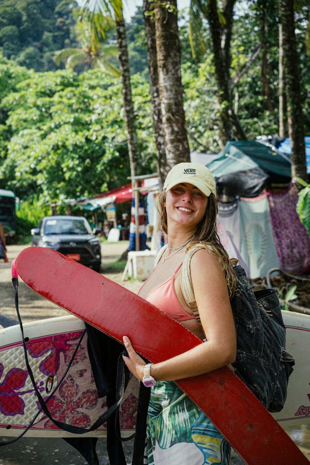 a woman holding a red surfboard next to a forest