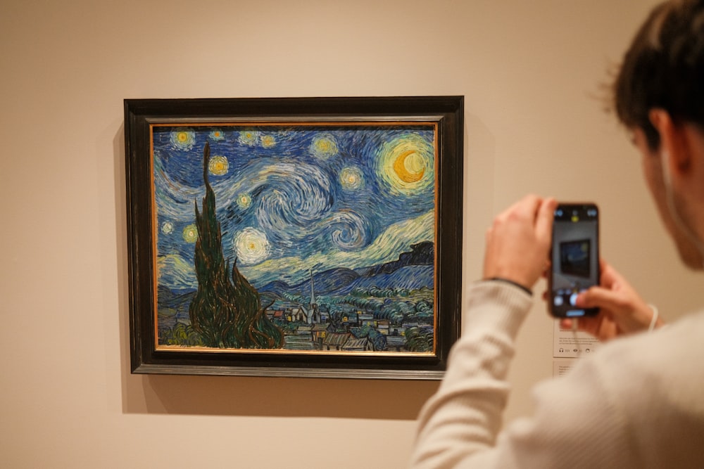 a woman taking a picture of a painting with a cell phone