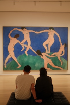 two people sitting on a bench in front of a painting