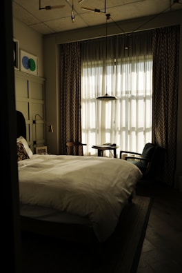 An elegant bedroom with large windows letting in natural light and soft linens.