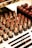 An assortment of lipsticks in various shades of red and brown is arranged in an organized manner. The lipsticks have black bases and gold holders, with some in open position revealing the color. Below them are makeup pencils with black and golden details, laid out neatly on a white surface.
