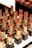 A display of various lipsticks, each housed in a gold and black casing, arranged neatly in rows. The lipsticks come in different shades of red and brown, and the background is slightly blurred, emphasizing the lipsticks.