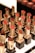 A display of various lipsticks, each housed in a gold and black casing, arranged neatly in rows. The lipsticks come in different shades of red and brown, and the background is slightly blurred, emphasizing the lipsticks.