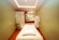 A serene and well-lit massage therapy room features a massage table adorned with scattered rose petals. The room has soft green walls with a floral accent wall in the back. A hanging white robe and a modern chair are present, along with a glass shower enclosure. The ceiling has recessed lighting, contributing to a calming atmosphere.
