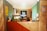 A reception area with a modern, earthy design features a wooden desk front, an aquarium with plants, and a prominent SNESAN logo in the background. The walls display multiple safety signs and instructions, and there's a small lamp and decorative items on the desk.