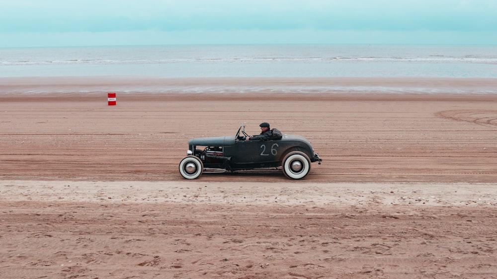 an old car driving on a beach near the ocean