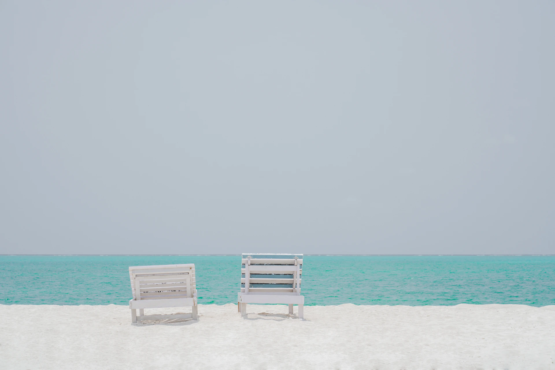 two white chairs sitting on top of a sandy beach