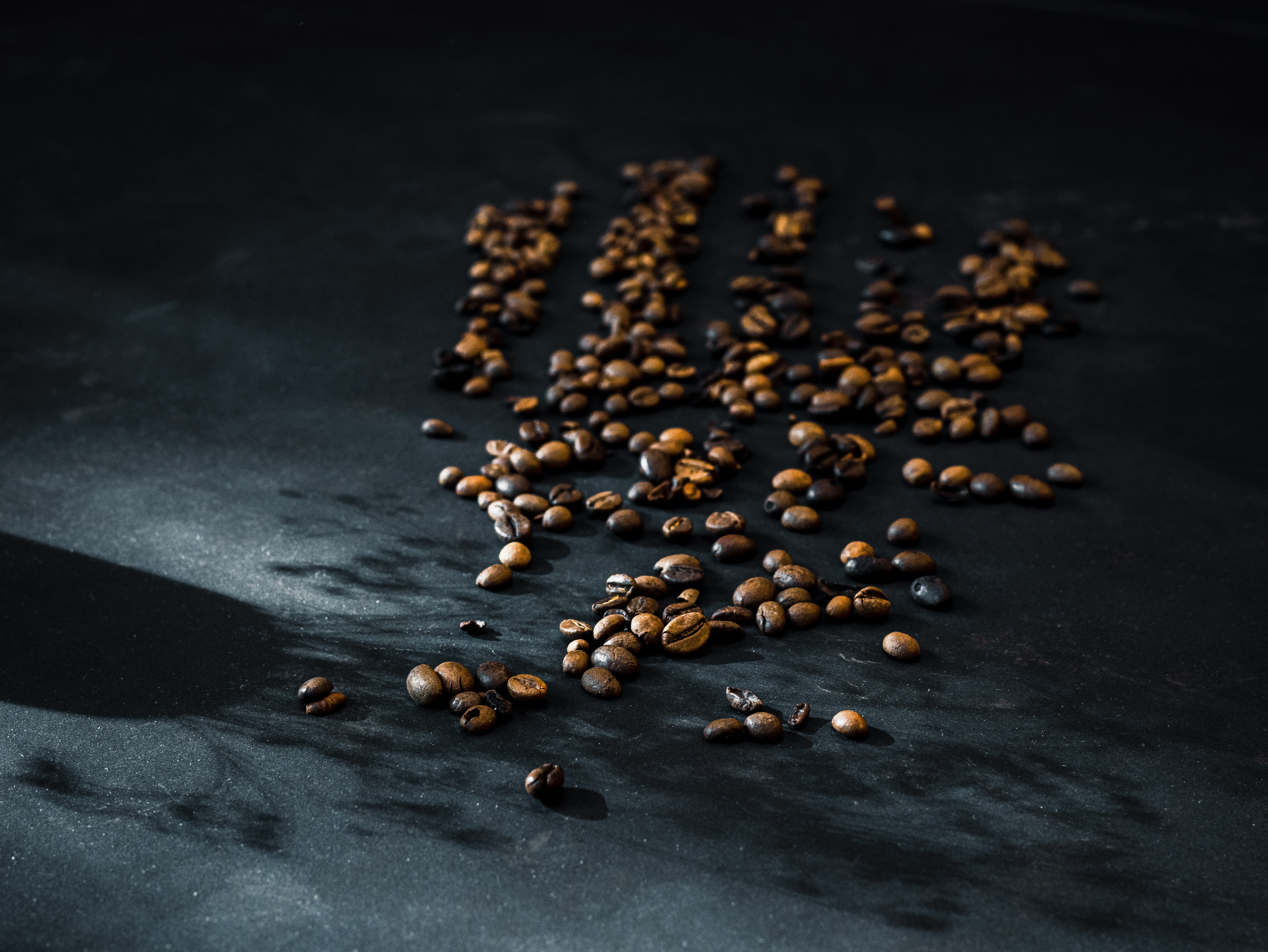 Overhead view of coffee beans scattered on a dark surface with dramatic lighting