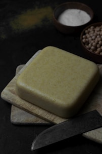 Golden blocks of homemade paneer stacked neatly on a rustic wooden board.