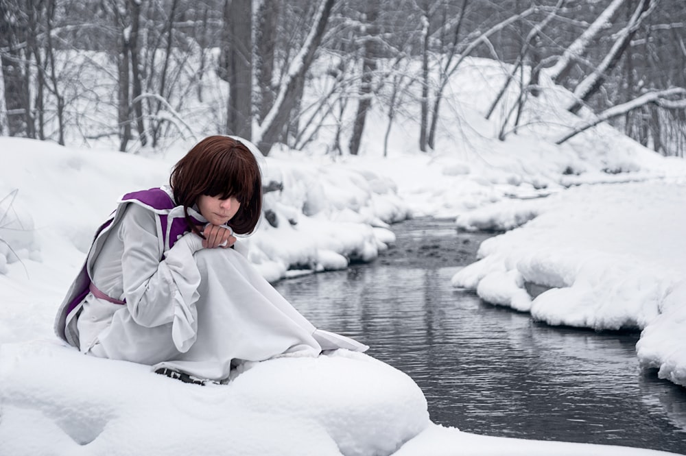 a woman sitting on a snow covered bank next to a stream