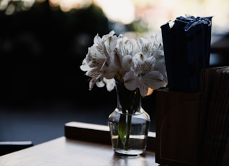A serene white lily arrangement resting gently on a polished wooden table, bathed in soft natural light.