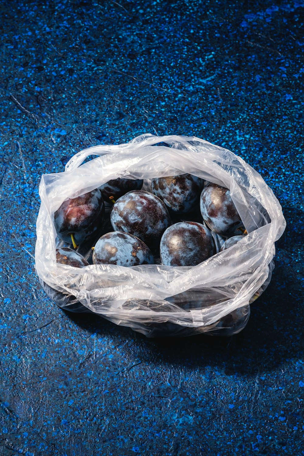 un sac en plastique rempli de prunes sur une surface bleue