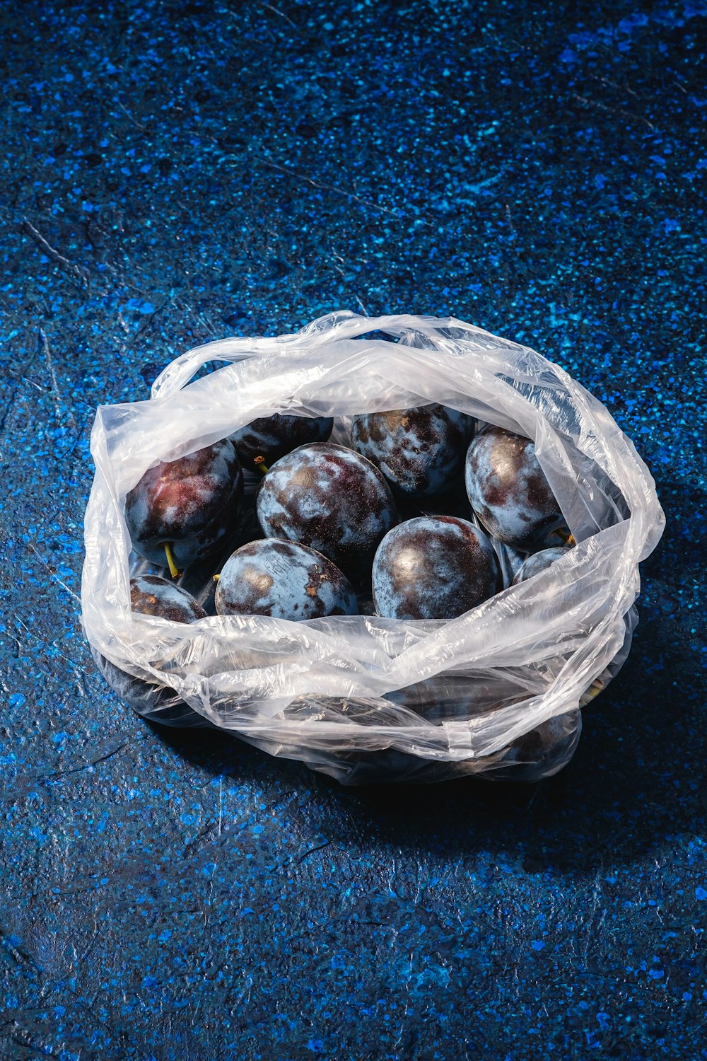 um saco plástico cheio de ameixas em uma superfície azul