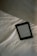 A digital e-reader device is placed on a white, wrinkled fabric surface, possibly a bed. Part of a grey fabric, which could be a blanket or a pillow, is visible in the top right corner. The e-reader screen displays text from an electronic book or document.
