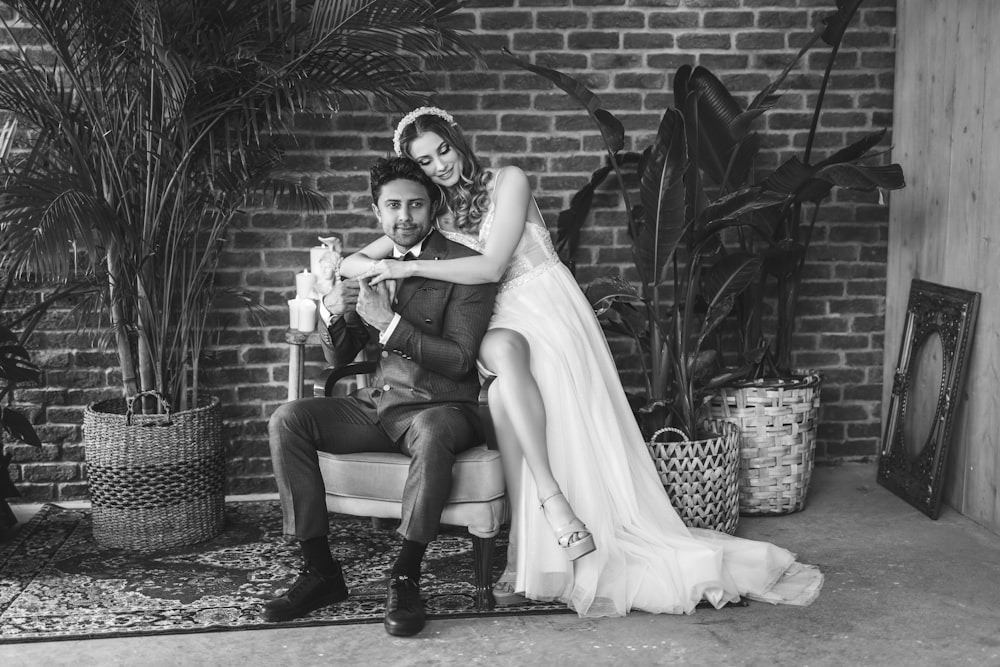 a bride and groom sitting on a chair in front of a brick wall