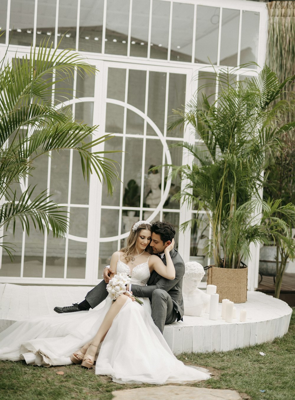 a bride and groom sitting on a bench in front of a building