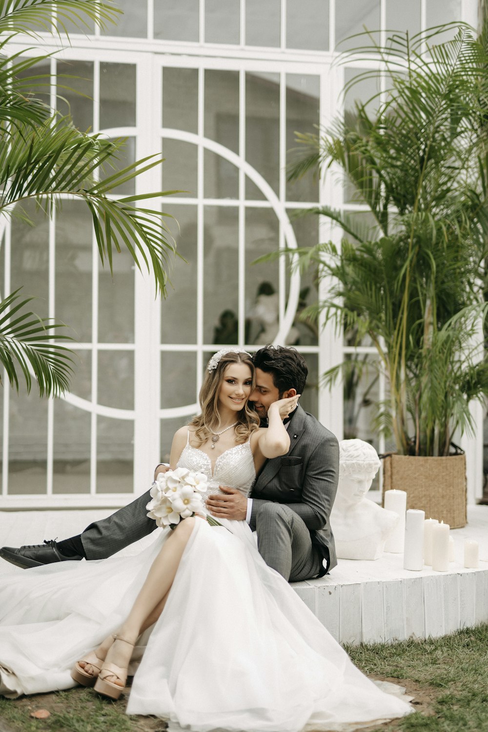 a bride and groom sitting on a bench in front of a building