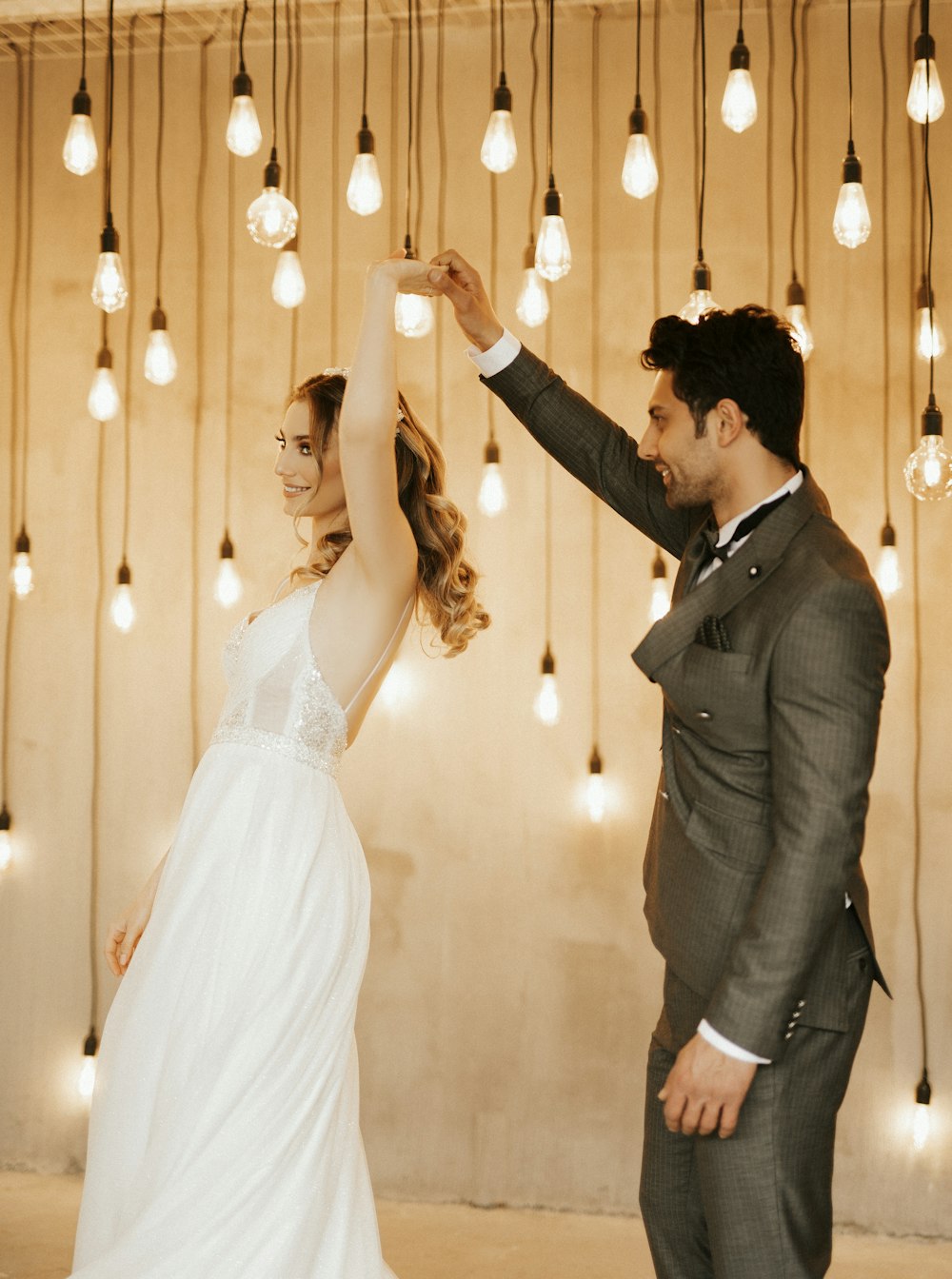 a bride and groom standing in front of a string of lights