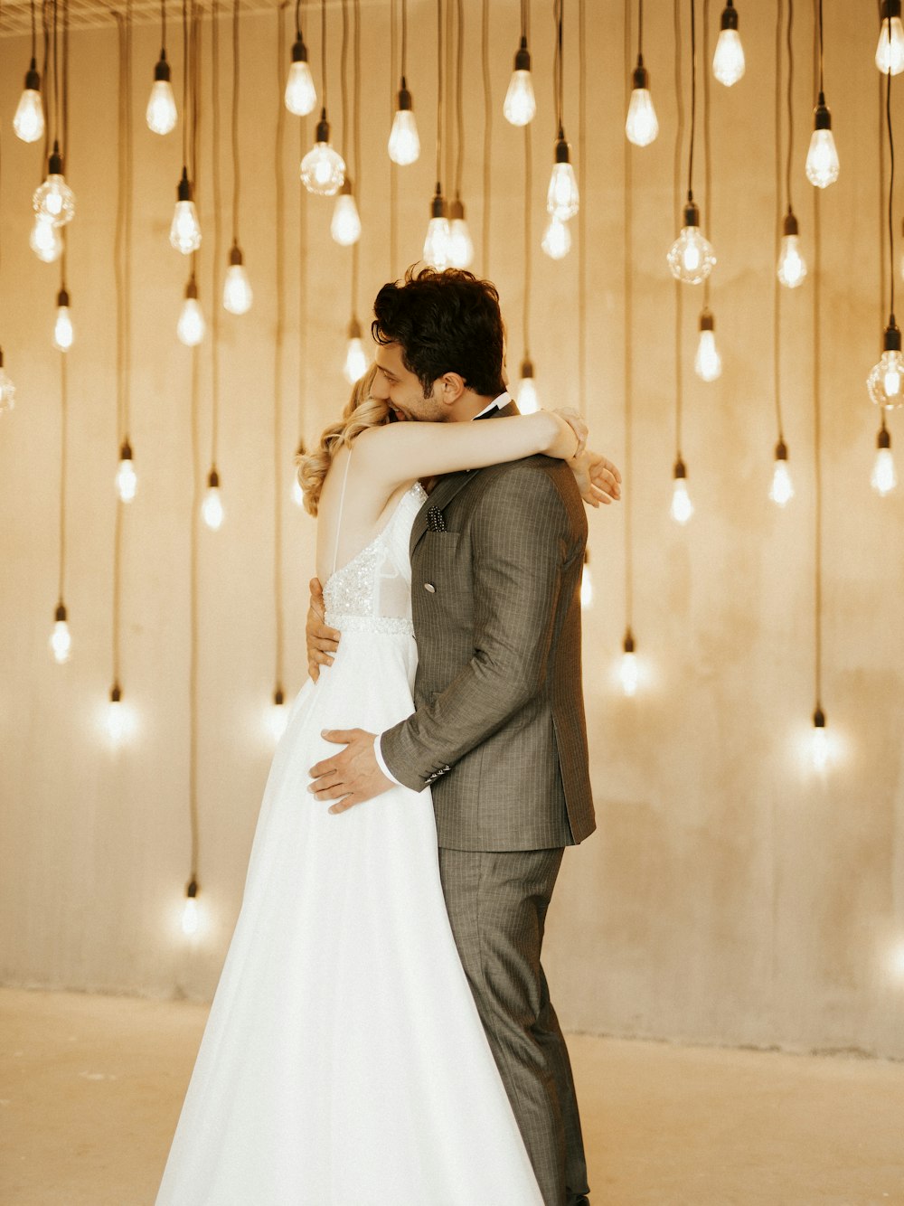 a bride and groom embrace in front of a string of lights