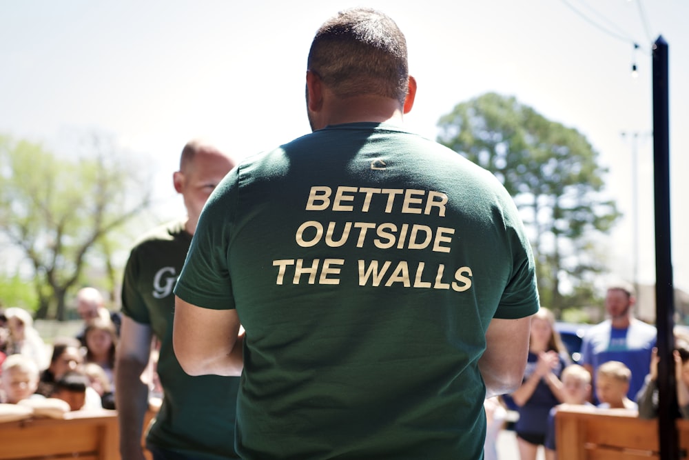 a man in a green t - shirt that says better outside the walls