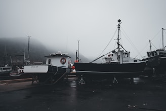 A misty sunrise over the Rías Baixas coastline with fishing boats docked.