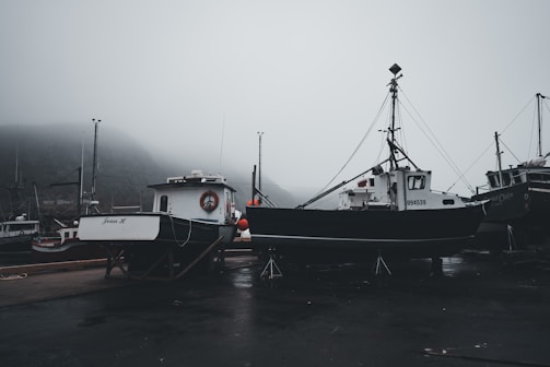 A misty sunrise over the Rías Baixas coastline with fishing boats docked.