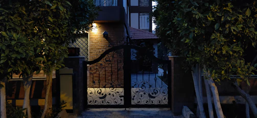 Evening view of a stainless steel gate glowing softly under warm outdoor lighting at a modern home entrance.
