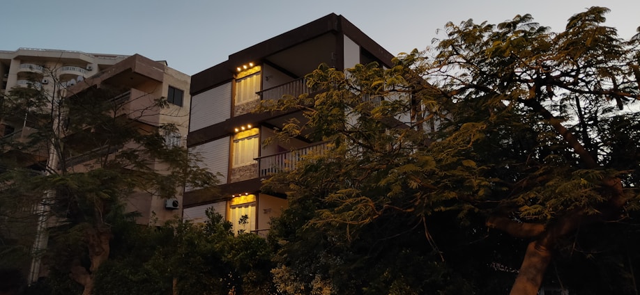 A modern residential building with warm lighting at sunset, surrounded by green trees.