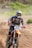 A motorcyclist wearing protective gear, including a helmet and goggles, rides a dirt bike at speed on a dirt track. The number 639 is visible on the front of the bike. The rider is surrounded by dirt and dust, with a blurred background of greenery.