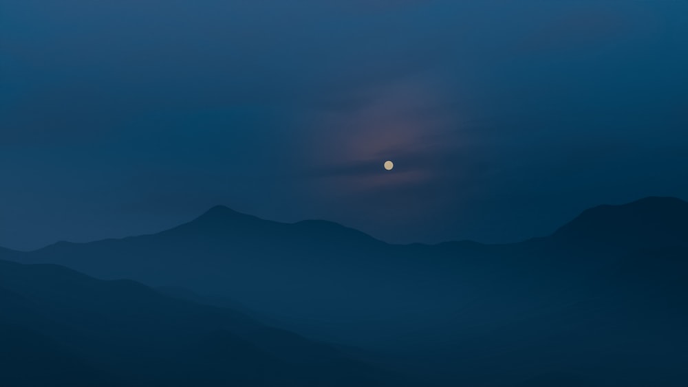 the moon is setting over the mountains in the distance