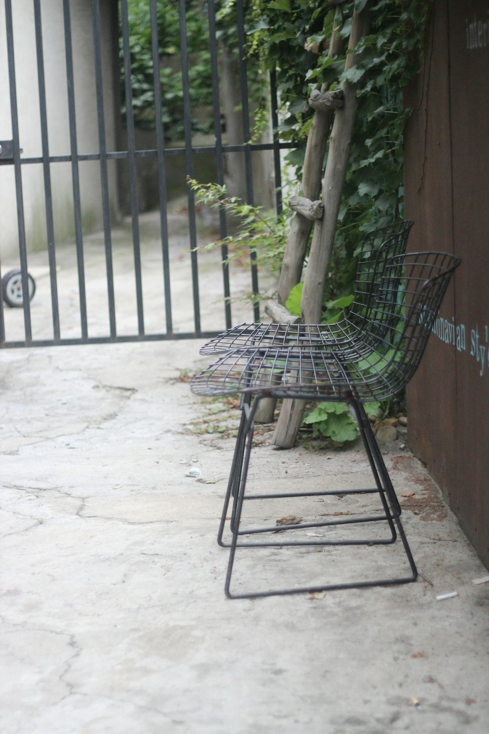 a metal chair sitting on a sidewalk next to a fence